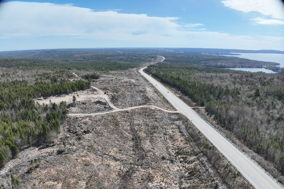 Aerial view of a road cutting through a forested area with a lake in the distance from a construction project.
