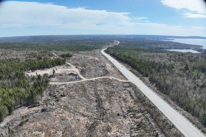 Aerial view of a road cutting through a forested area with a lake in the distance from a construction project.