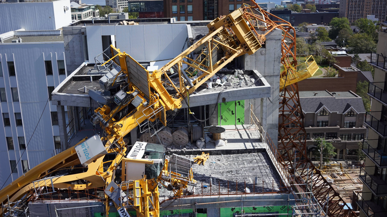 Large yellow crane seen fallen onto a residential tower after a wind storm, view from a drone next to the building.