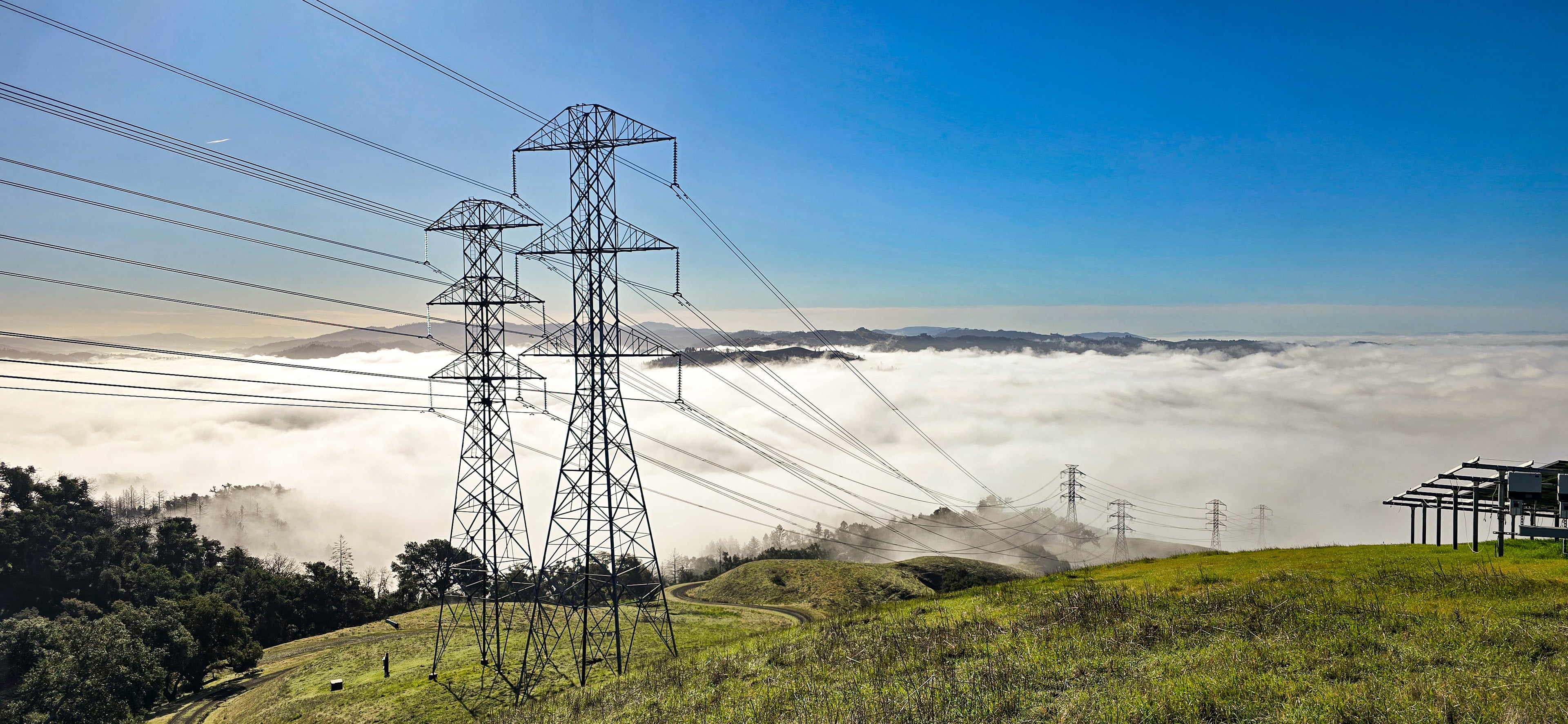 Power transmission lines with towers on a grassy hillside under a clear blue sky.
