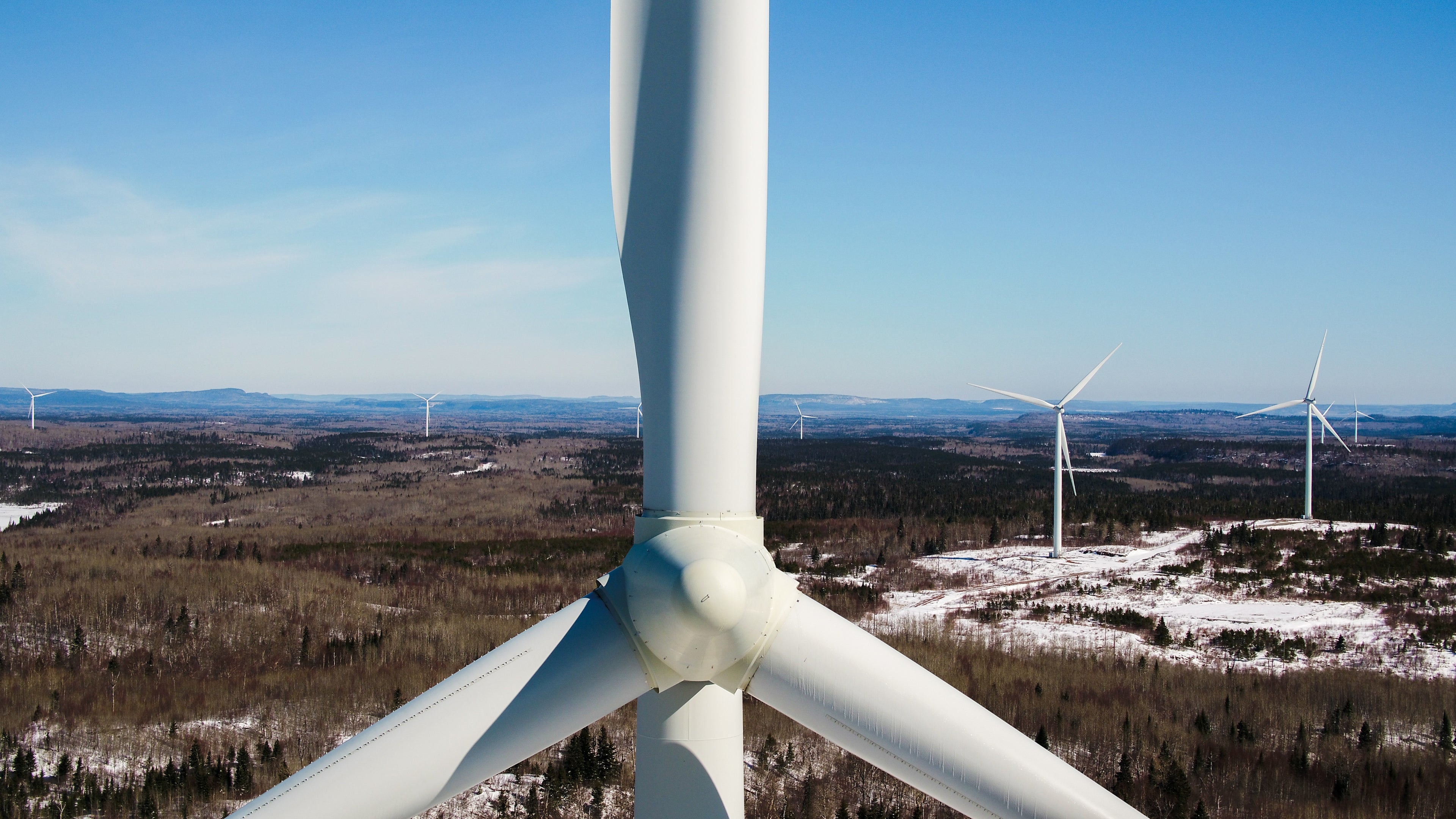 Close-up of a wind turbine, a field of wind turbines can be seen in the background