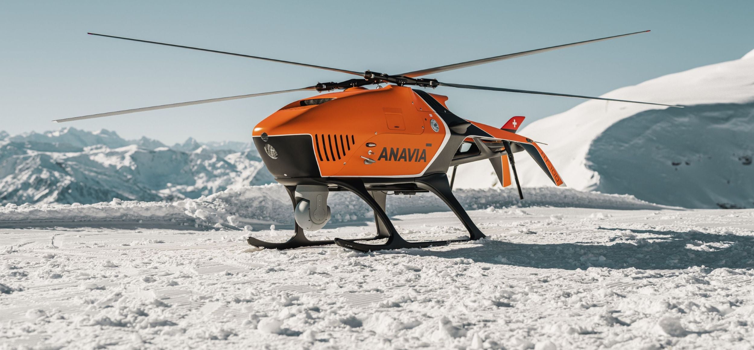 Orange HT-100 helicopter on a snowy landscape with mountains in the background