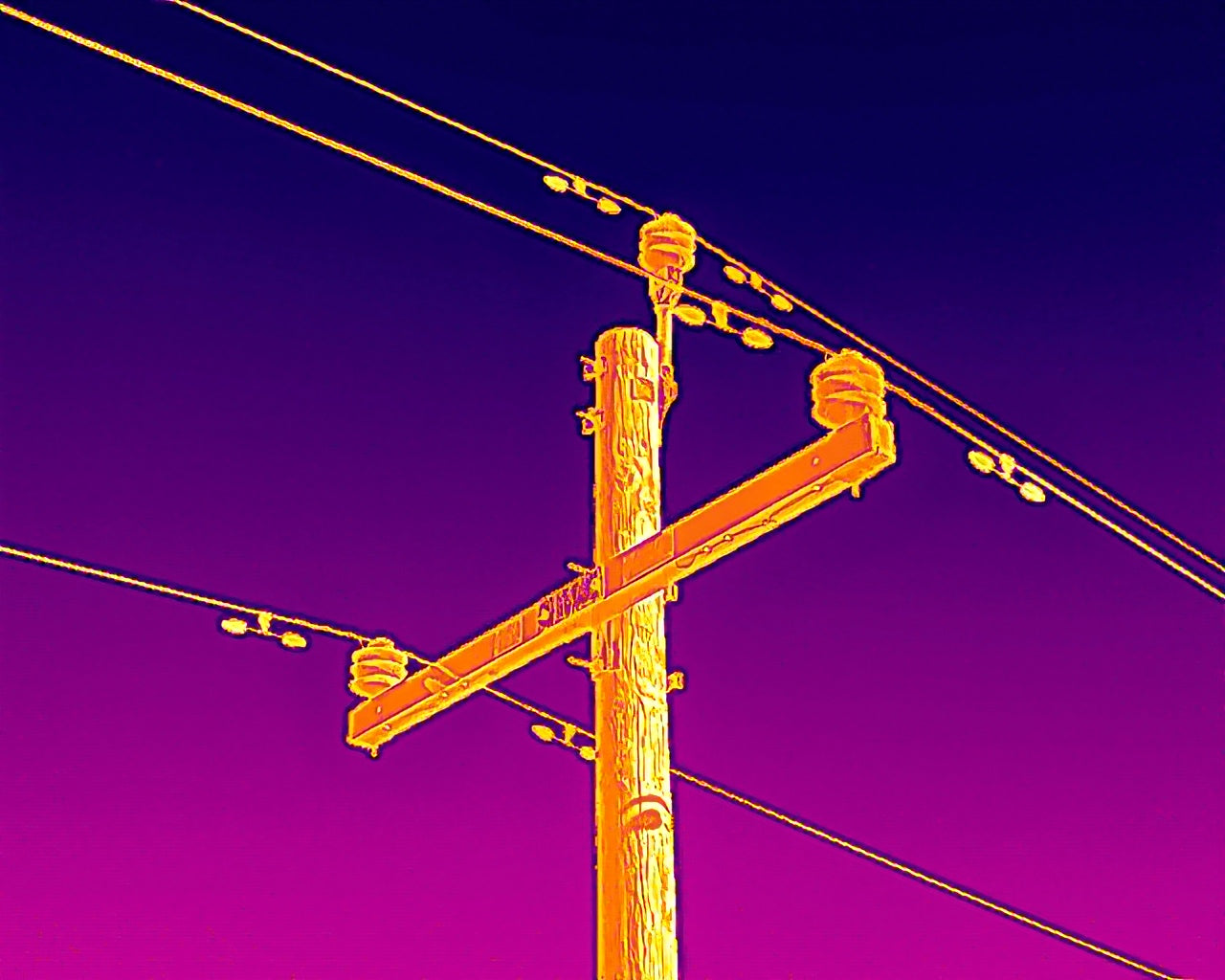 Thermal imaging of a wooden power pole with electrical wires.